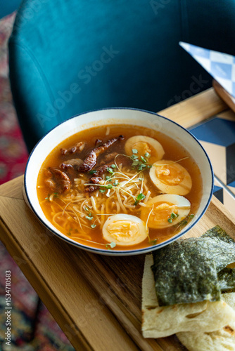 A comforting bowl of noodle soup filled with tender beef slices and perfectly soft boiled eggs. Accompanied by crispy seaweed, this dish invites warmth and flavor in a stylish setting