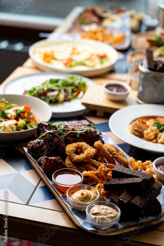 An enticing spread of dishes fills the wooden table, featuring crispy appetizers, fresh salads, and hearty entrees. Diners are drawn to the colorful presentation and rich aromas