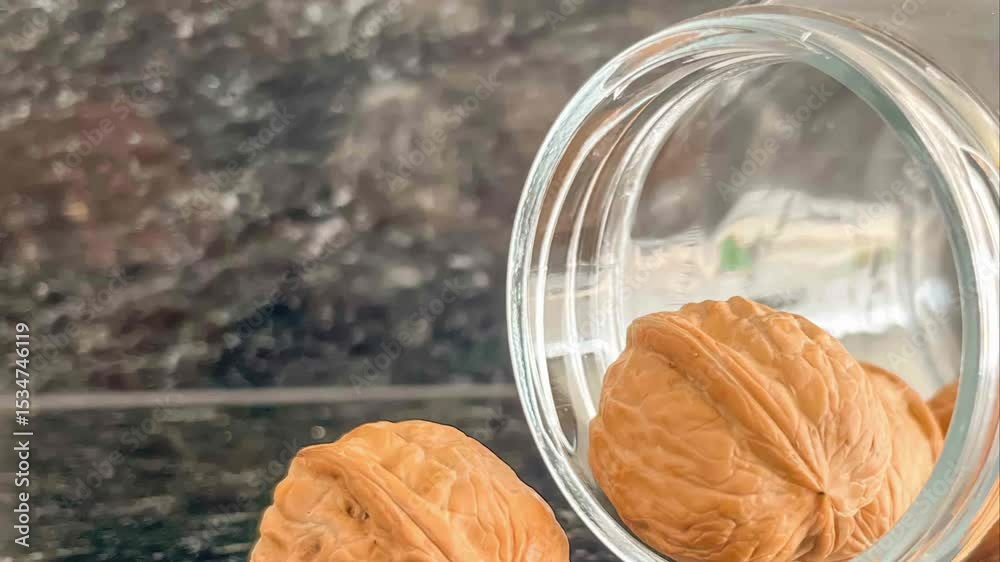 A close up of walnuts spilling from a glass jar on a dark marbled surface in soft diffused light