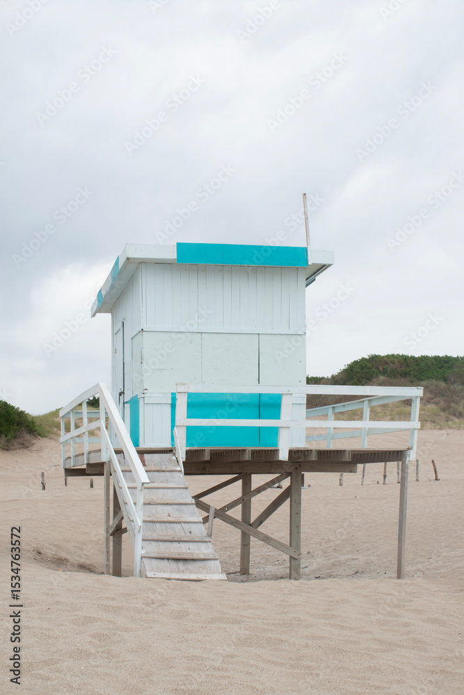 Obraz premium On a sunless day, the light blue and white lifeguard cabin contrasts with the dune landscape.