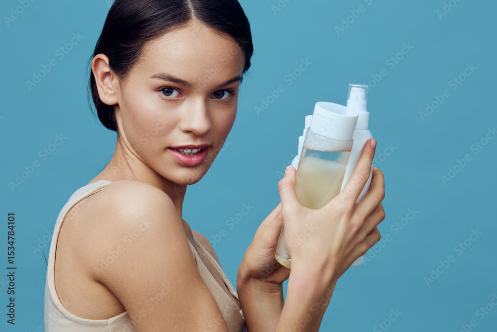 Young woman with a natural look holding skincare products against a blue background, emphasizing beauty and self care for healthy skin Young woman with a natural look holding skincare products against a blue background, emphasizing beauty and self care for healthy skin