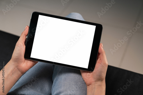 Hand holding digital tablet with blank screen for graphic display montage on the sofa in the living room, mockup display for lifestyle and wireless technology.