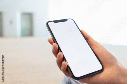 Hand holding smartphone with blank screen for graphic display montage on outdoors background, mockup display for lifestyle and wireless technology.