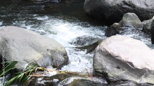 Camera zooms out over a view of a river with clear water and volcanic rocks