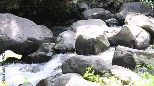Camera zooms in over a view of a river with clear water and volcanic rocks