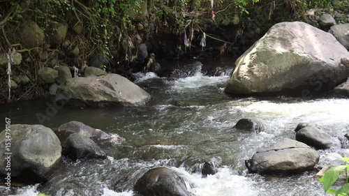 Camera zooms in over a view of a river with clear water and volcanic rocks
