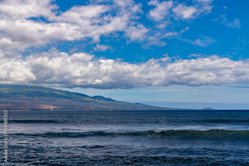 Ocean view of Maui with blue sky and clouds, and a sailboat.