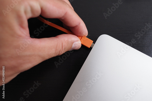 Hand connected laptop with orange color USB cable. 