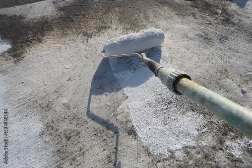 Painter applying a fresh white waterproof coat paint with a roller tool to a roof surface. POV.