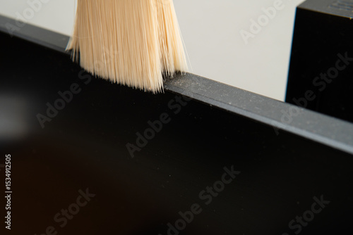 Detailed macro photograph of soft brush cleaning dust from a black electronic device screen for tech maintenance or household care concept