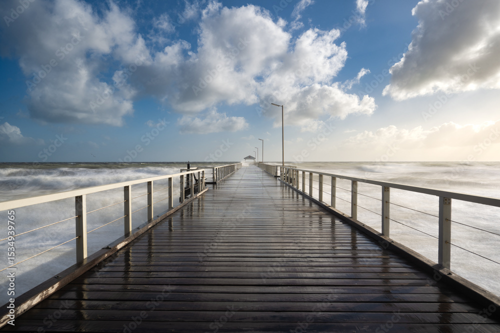 Fototapeta premium Henley jetty, Adelaide South Australia, long exposure ocean waves with timber jetty extending into distance, dramatic clouds in blue sky