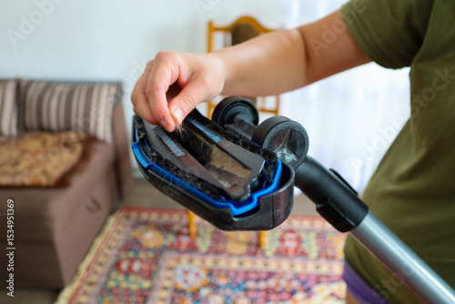 A diligent person meticulously cleans the vacuum cleaner nozzle of hair and dirt. This action emphasizes the importance of maintaining household appliances and striving for cleanliness in the home.