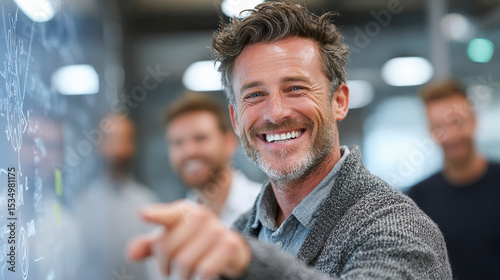 Fundamentals of Leadership : A smiling man pointing at a whiteboard during a collaborative meeting with male colleagues standing in the background.