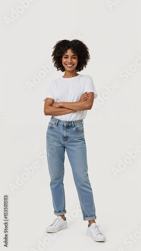 Full length of confident Ethiopian girl smiling in a casual outfit in a white tshirt and jeans standing with her arm and leg crossed on plain white background