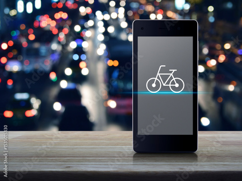 Bicycle flat icon on modern smart phone mobile screen on wooden table over blur colorful night light city road and cars, Bike shop online concept