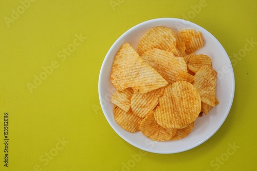 Potato chips in white plate on yellow background