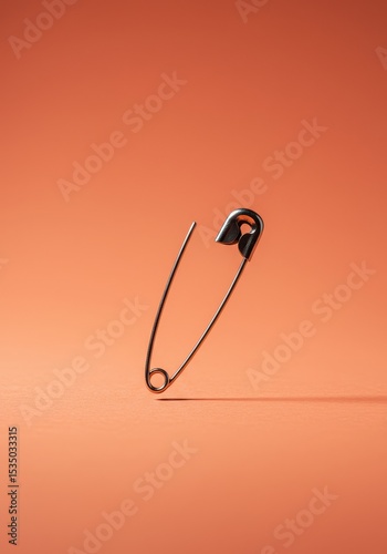 Open safety pin standing upright on orange surface with strong shadow