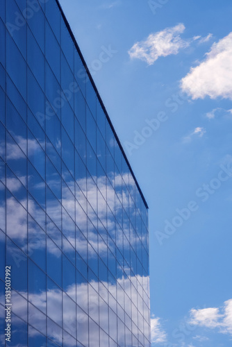 Fotografija Blue sky and white clouds are reflected in the glass wall of a tall modern building