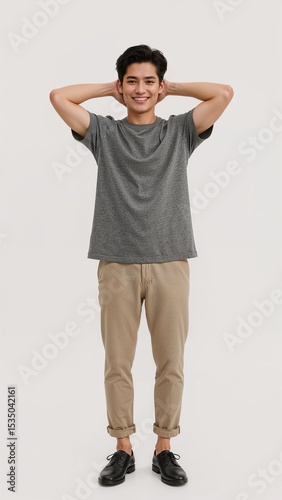 Full length of confident Singaporean man in a casual tee and rolledup chinos standing with hands behind his head and grinning on plain white background