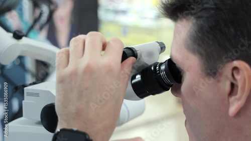 Man using microscope for close examination. Close-up of a man looking through a binocular microscope, adjusting focus during a detailed observation in a clinical or lab setting.