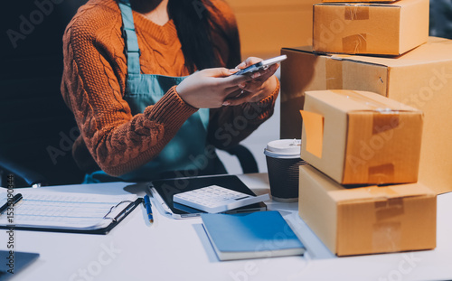 Startup SME small business entrepreneur of freelance Asian woman wearing apron using laptop and box to receive and review orders online to prepare to pack sell to customers, online sme business ideas.