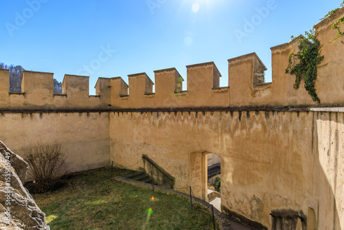 Historic stone fortress wall under clear blue sky with sunlit battlements