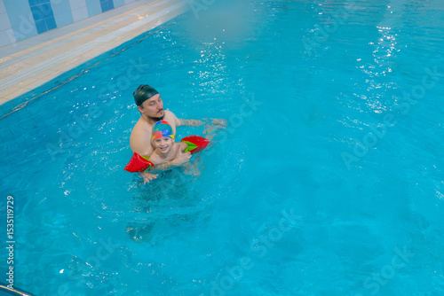 Happy middle-aged father swimming with cute adorable baby in swimming pool. Smiling dad and little child, boy having fun together. Active family spending leisure and time in spa hotel. Concept of kids