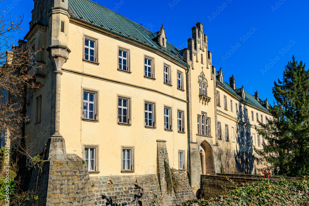 Fototapeta premium Historic gothic revival castle with stone facade and ivy-covered walls under clear blue sky