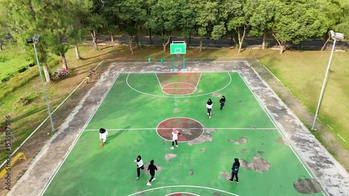 Aerial view of women playing basketball on a green and red court outdoors
