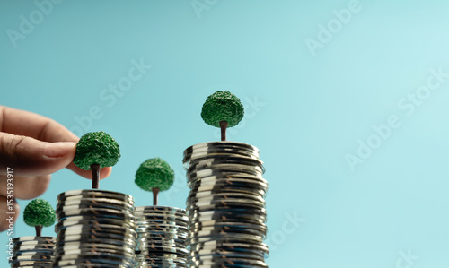Hand putting Mini trees to growing on coin stacks symbolizing sustainable investment, green finance, and eco-friendly economic growth