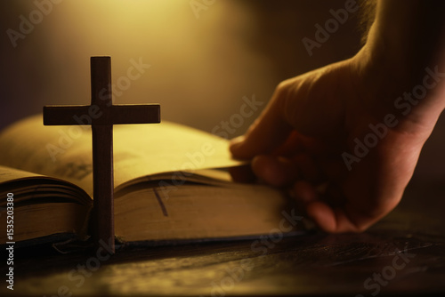 Hand Turning Page of Bible with Wooden Cross Under Warm Light
