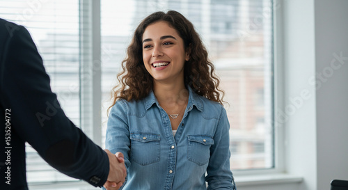 Free Download Smiling woman shaking hands with a person in a professional setting, near a window. - GFXLoad