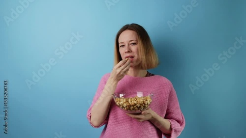 Happy female eating popcorn, cheerful emotion, pink sweater and background.