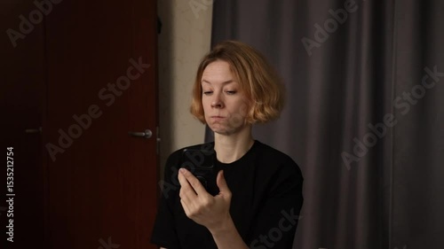 Angry woman with phone at home, reacting to stressful news, displaying annoyance and distress.