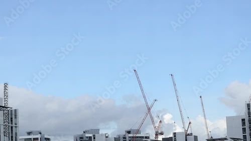 Time lapse of white and dark clouds moving against blue sky before rain with construction cranes in foreground. Summer nature weather sky. 