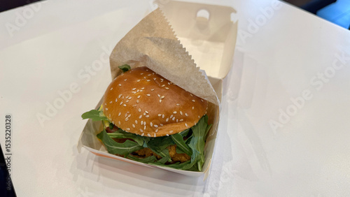 Fotografie sesame seed bun burger wrapped partially in paper on a white table