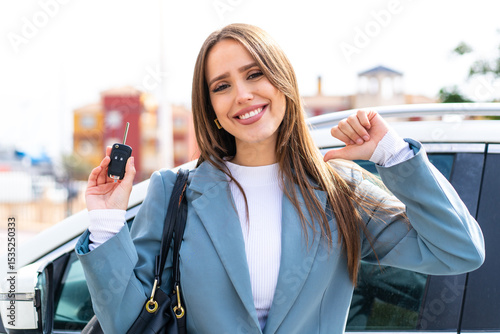 Young pretty woman holding car keys at outdoors proud and self-satisfied