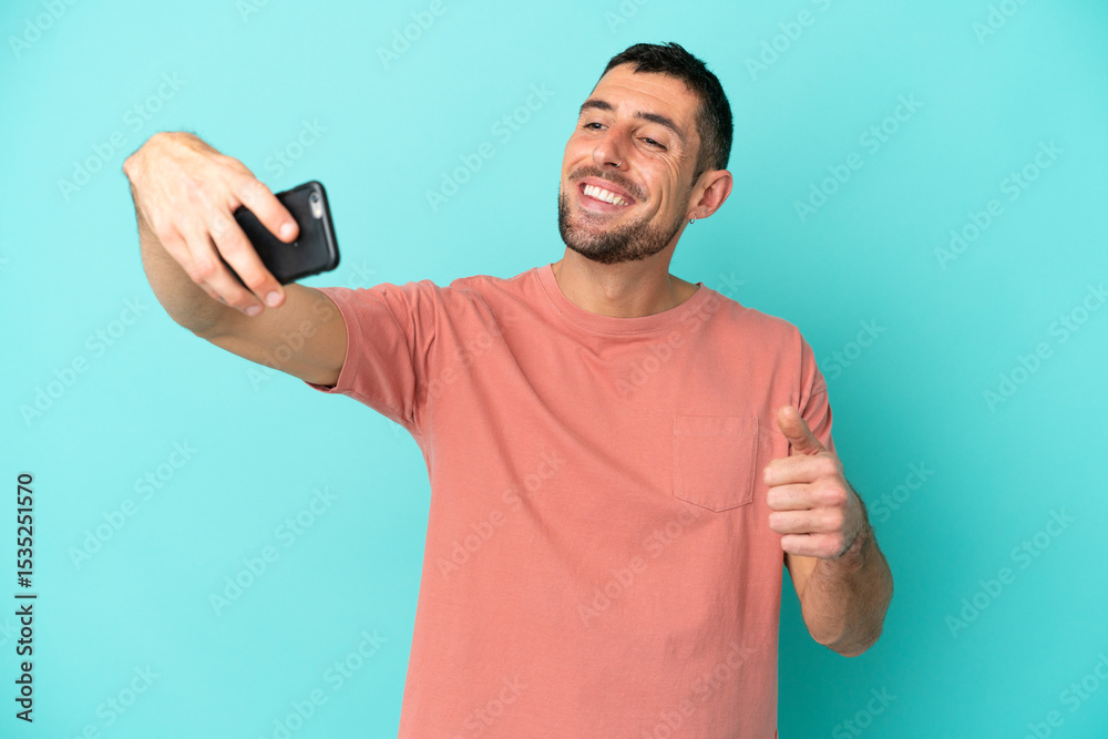Fototapeta premium Young handsome caucasian man isolated on blue background making a selfie with mobile phone