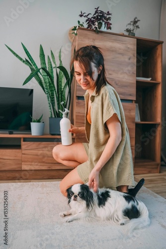 woman kneeling on carpet spraying houseplants, wooden tv cabinet with small japanese chin dog looking at her, daylight, eco living, home styling, pet care, vertical