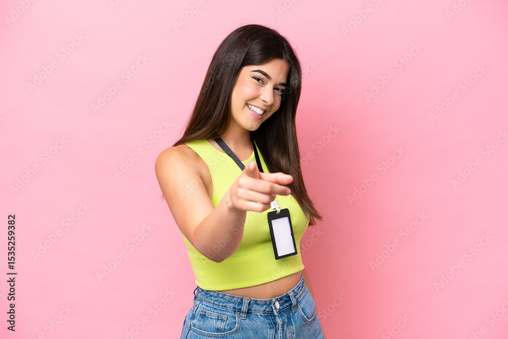 Young Brazilian woman with ID card isolated on pink background pointing front with happy expression Young Brazilian woman with ID card isolated on pink background pointing front with happy expression