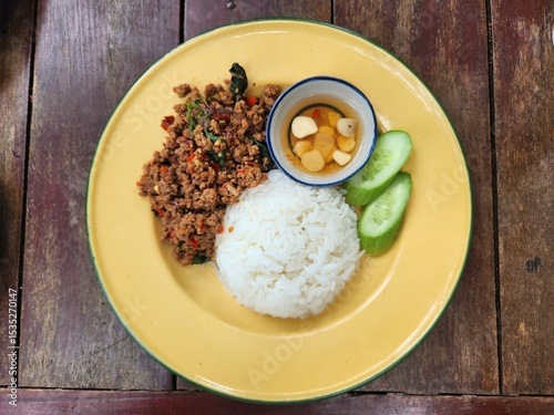 Spicy Thai basil beef stir-fry served on a yellow plate placed on a rustic wooden table.