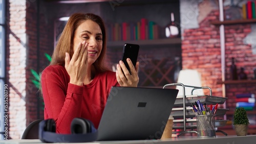Woman freelancer taking online course to develop new skills from home office, attend online video call and watching lecture on smartphone. Lady participates at virtual training class. Camera A.