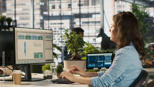 Accountant in busy modern startup agency imputing financial figures on PC after checking reports. Focused businesswoman working in modern office, crosschecking data, camera A
