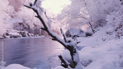 Bare snowy branch beside calm winter river under pinkish dusk sky surrounded by frost-covered trees. Nature concept