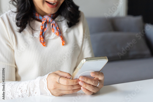 Closeup hands of happy smiling young woman using smartphone to social media online at home. Young woman looking at cellphone holding mobile cell phone chat message