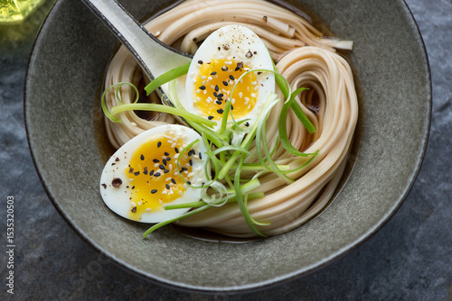 Bowl of udon noodles with boiled chicken egg and spring onion, middle closeup, horizontal shot, selective focus