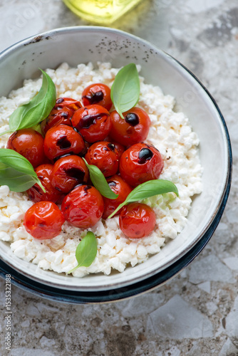 Caprese with cottage cheese, roasted cherry tomatoes and fresh basil in a grey bowl, vertical shot on a brown granite surface, middle closeup