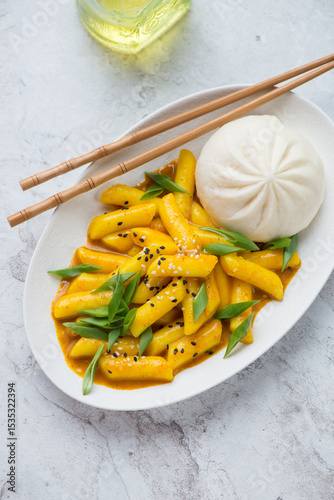 Plate with korean tteokbokki or garaetteok and steamed baozi bun, vertical shot on a white stone background, high angle view