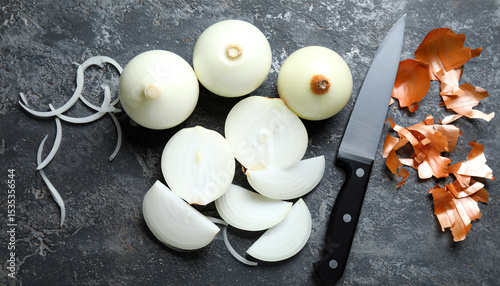 A rustic kitchen scene featuring sliced onions, a knife, and onion peels on a dark textured surface.