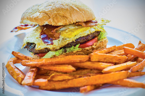 breakfast burger topped with lettuce, tomato, bacon, and a fried egg served with sweet potato fries
